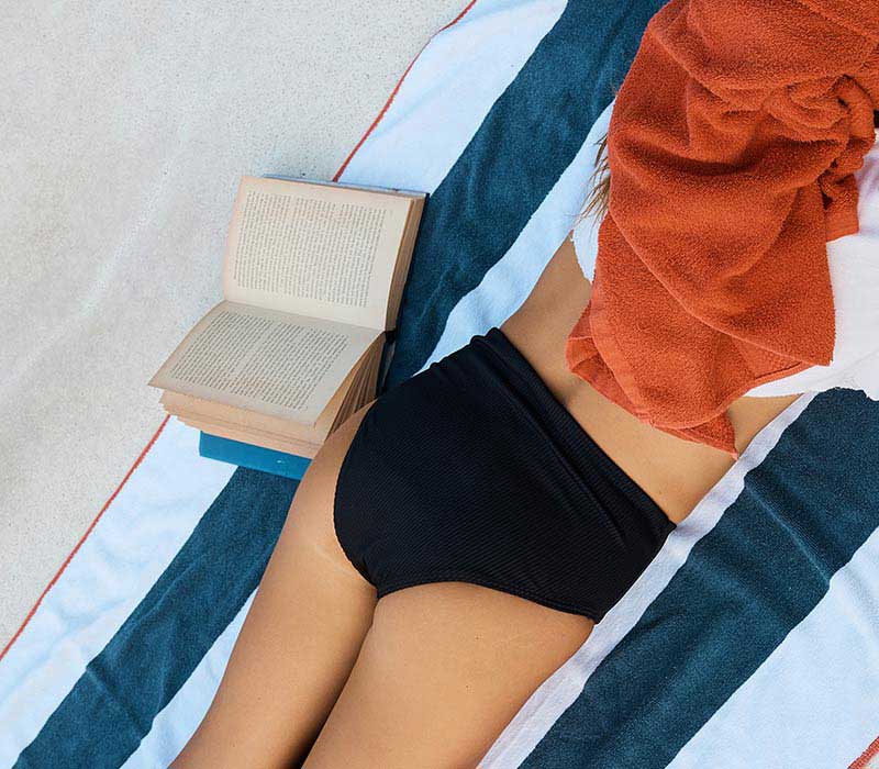 Girl on towel on sand wearing Scarlet Period leakproof Swim Briefs