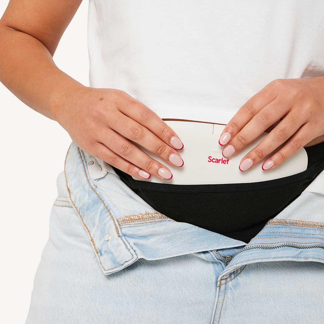 Hands settling the white rae heat pad into a black Scarlet pocket brief under open jeans