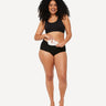 Woman in black Scarlet underwear sliding the white rae heat pad into the pocket of her brief